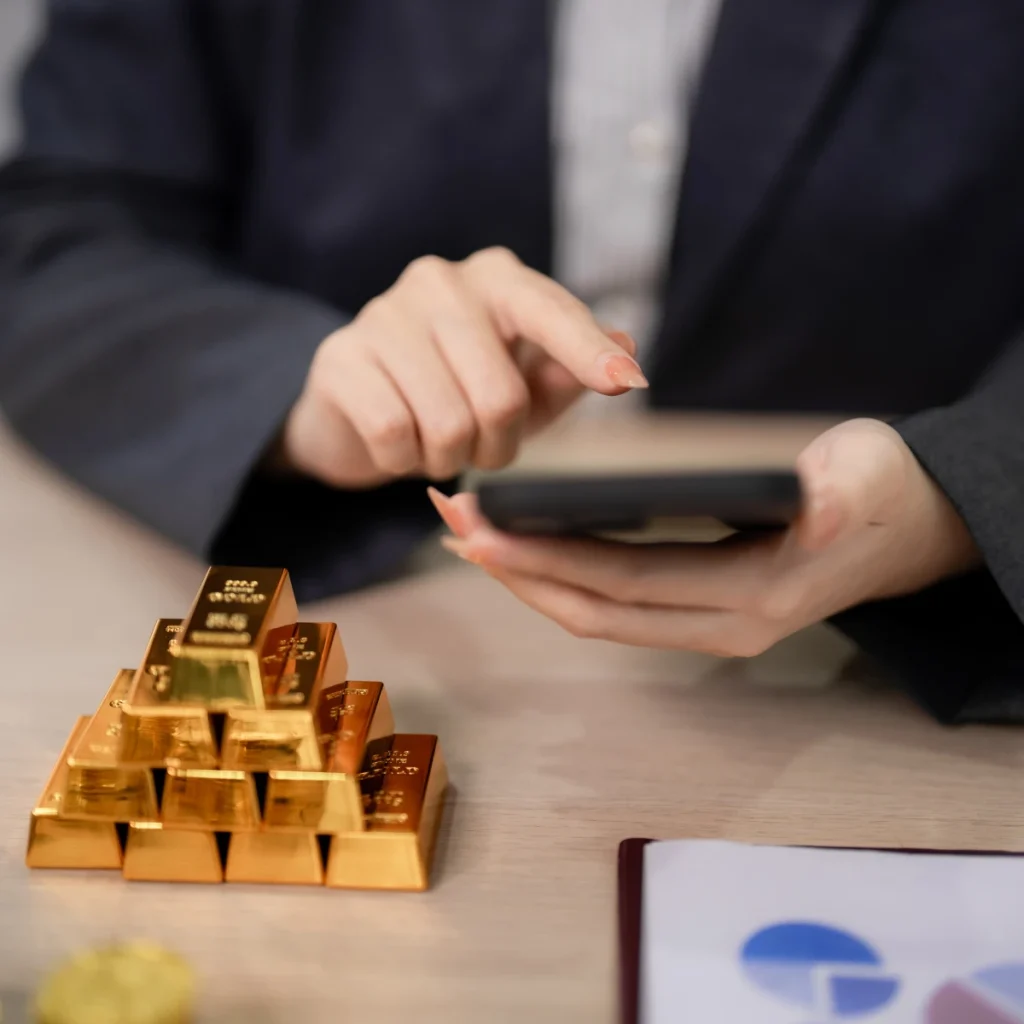 Geschäftsperson nutzt Smartphone neben gestapelten physischen Goldbarren für institutionelles Goldinvestment.